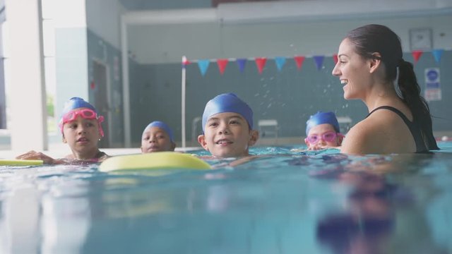 Female Coach In Water With Children Gives Swimming Lesson In Indoor Pool