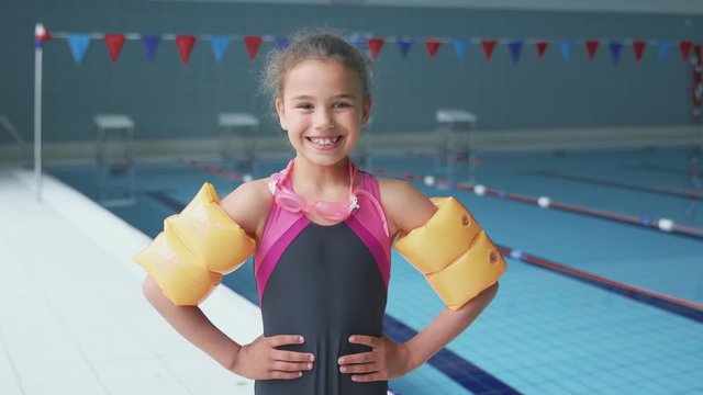 Portrait Of Girl Standing By Edge Of Swimming Pool Ready For Lesson