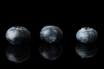 Group of three whole fresh blue blueberry isolated on black glass