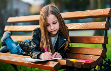 Cute girl enjoying in the park while drawing with a felt pen. Lifestyle, childhood, education concept