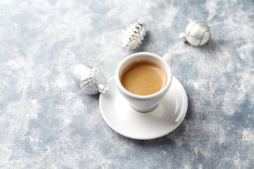 Cup of coffee and silver Christmas baubles on bright wooden background. Copy space.