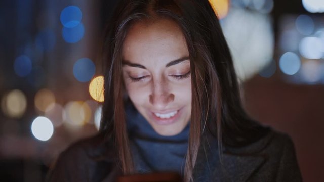 Closeup of prety smiling woman using smartphone walking at night city, slowmotion fullHD stock footage, handheld camera shot