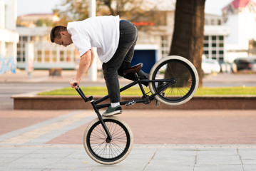The guy on the BMX bike performs a trick on the front wheel.