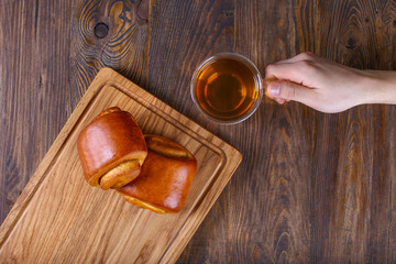 Two tasty buns in hands. Black tea. Delicious breakfast on wooden table.Close up