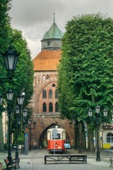 ulica w centrum starego Słupska, gotycka brama miejska, dawne więzienie, obecnie galeria sztuki Nowa Brama, zabytkowy tramwaj na torze - obrazy, fototapety, plakaty