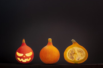 Three little pumpkins with halloween face lie in a line on a gray background. One pumpkin cut with seeds inside. Red pumpkin first on the left. Copy space. Vignette.