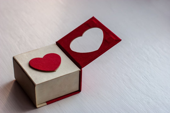 White gift box with a red heart on the lid for a romantic gift for girls on a painted wooden surface. One half of the lid is open. The heart is cut in the lid. Magnet cover. Copy space.