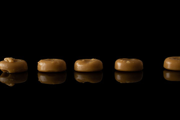 Lot of whole caramel brown candy in row isolated on black glass