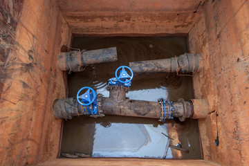 Rupture of a water pipe in a square well with water. Blue valves with taps. Urgent repair. Flange...
