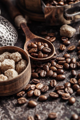 Coffee beans in wooden spoon on dark textured background.