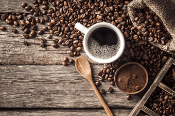 Coffee cup with coffee beans on wood background.
