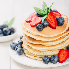 Classic american pancakes with fresh berry on white wood background. Summer homemade breakfast.