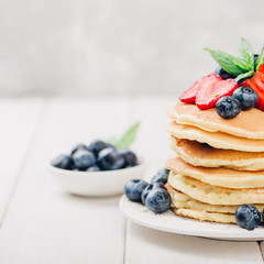 Classic american pancakes with fresh berry on white wood background. Summer homemade breakfast.