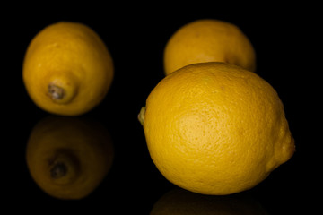 Group of three whole fresh yellow lemon disordered isolated on black glass