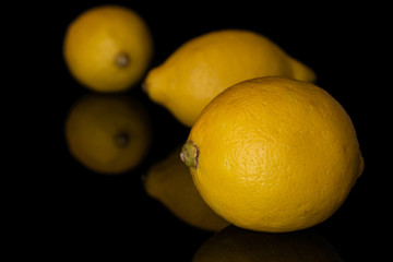 Group of three whole fresh yellow lemon disordered isolated on black glass