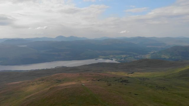 An aerial forward footage of a grassy mountain plateau with a huge lake and mountain range in the background under a cloudy sky 