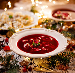 Christmas beetroot soup, red borscht with small dumplings with mushroom filling in a ceramic white plate on a holiday table.Traditional Christmas eve dish in Poland. 