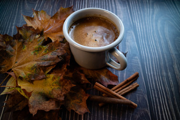 Cafe latte with some sticks of cinnamon and autumn leaves. Close up view on wooden table. Blogging concept.