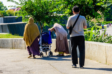 Muslim man with his wives and baby carriage walking in a city park