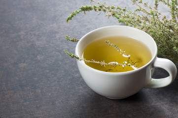 White cup of healthy herbal thyme tea with fresh thyme leaves bunch on grey rustic background, hot drink thymus vulgaris