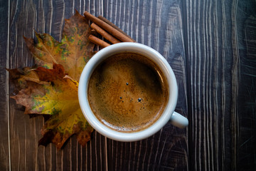 Warm coffee in the morning on a wooden table with fall leaves and cinamon
