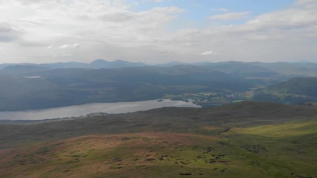 An aerial backward footage of a grassy mountain plateau with a huge lake and mountain range in the background under a cloudy sky 