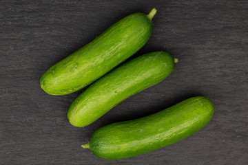 Group of three whole mini green cucumber flatlay on grey stone