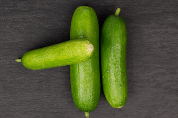 Group of three whole mini green cucumber flatlay on grey stone
