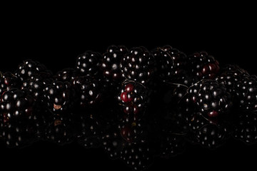 Lot of whole arranged fresh black blackberry isolated on black glass