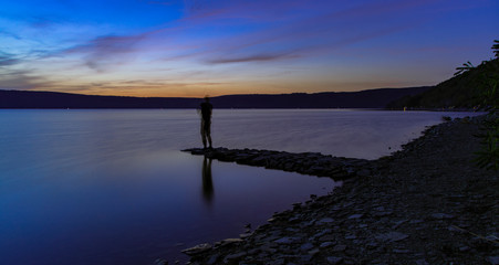 abstract unfocused human silhouette fishing life style hobby action in peaceful twilight lake shore line scenic landscape after sunset, concept long exposure photography with empty copy space 