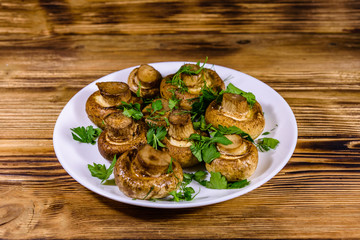 Plate with baked champignons, dill and parsley on a wooden table