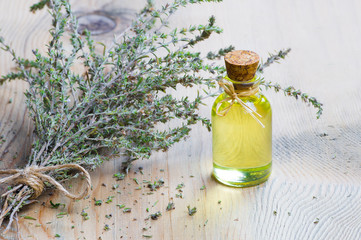 glass bottle of thyme essential oil and bunch of dry thyme on wooden rustic background. Dried spice...