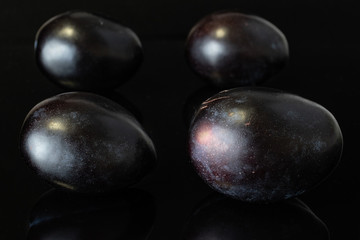 Group of four whole fresh purple plum isolated on black glass