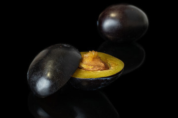 Group of one whole two halves of fresh purple plum isolated on black glass