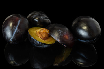 Group of three whole two halves of fresh purple plum isolated on black glass