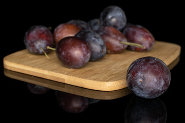 Lot of whole sweet purple plum front focus on bamboo cutting board isolated on black glass