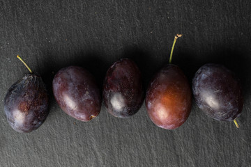 Group of five whole sweet purple plum flatlay on grey stone