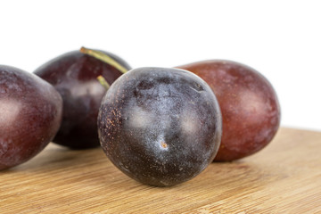 Group of four whole sweet purple plum on bamboo cutting board isolated on white background