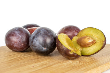 Group of four whole two halves of sweet purple plum on bamboo cutting board isolated on white background