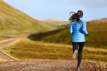 Running woman on trail run doing fitness exercise in spring autumn mountains. Person training outside in cold weather in blue sportswear.