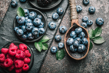 Fresh berries with raspberries, blueberries, blackberries in bowl on a stone stand on a dark metal background.