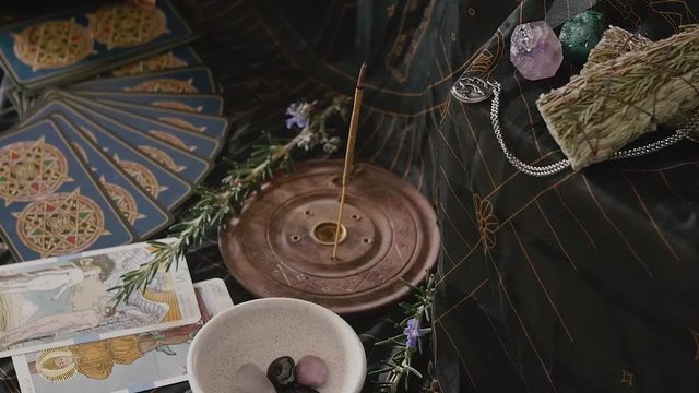 Slow zoom in of altar with esoteric items like rosemary, incense, gemstones, sage