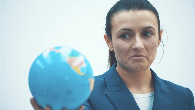 Close-up of a young teacher on a white background. Holds the globe. Has a surprised facial expression.