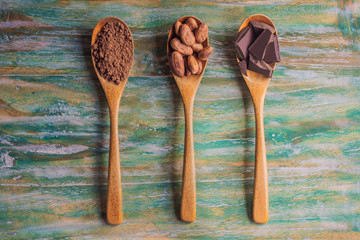 Spoons with cocoa powder, cocoa beans and pieces of chocolate