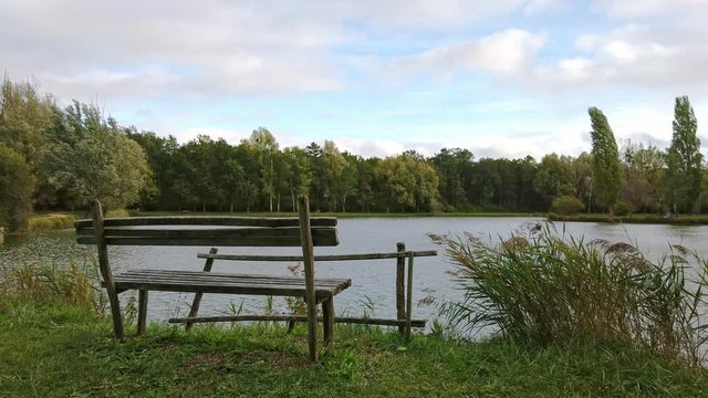 View of a wooden bench at the edge of a lake with a lot of wind