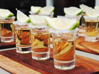 Tequila shots with lime and salt on the wooden tray.
