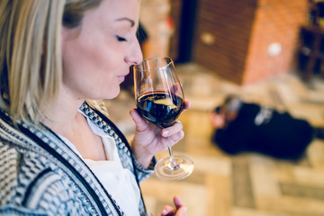 Young blonde woman holding a glass of red vine at home or the restaurant smelling before taste at the party