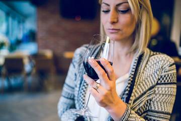 Young blonde woman holding a glass of red vine looking at beverage at party home or restaurant celebration holiday