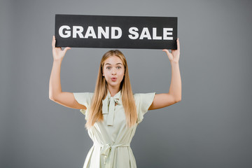 surprised young blonde pretty girl with grand sale sign isolated over grey