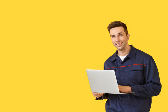 Male car mechanic with laptop on color background